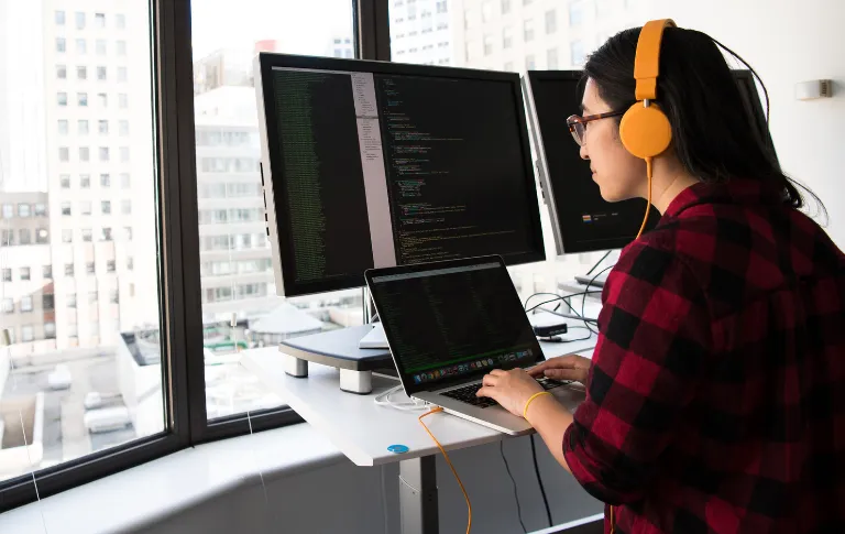 Programmatrice asiatica in piedi di fronte a schermi con codice